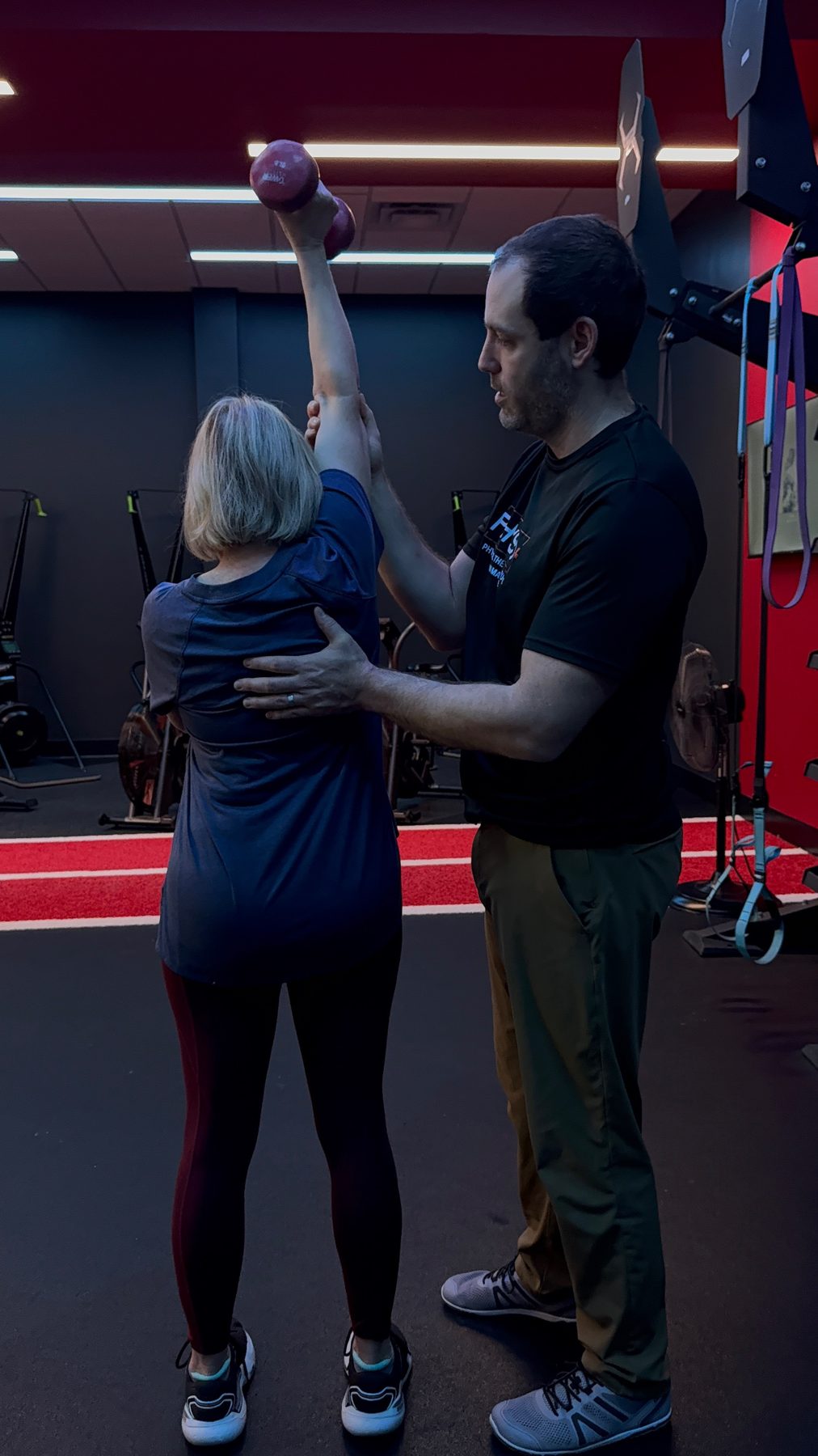 Overhead dumbbell press with hands on shoulder support at Physio+